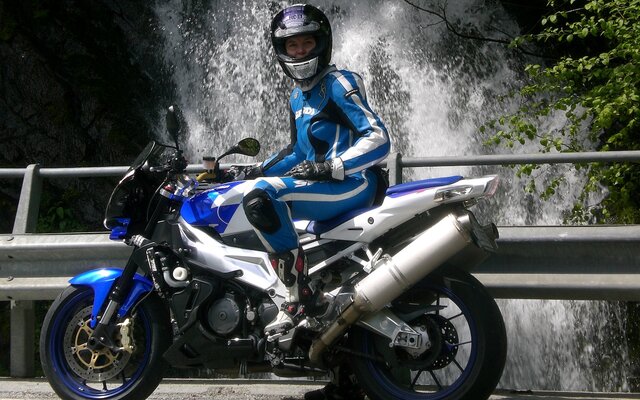 Motorradfahrerin in blauem Anzug vor Wasserfall