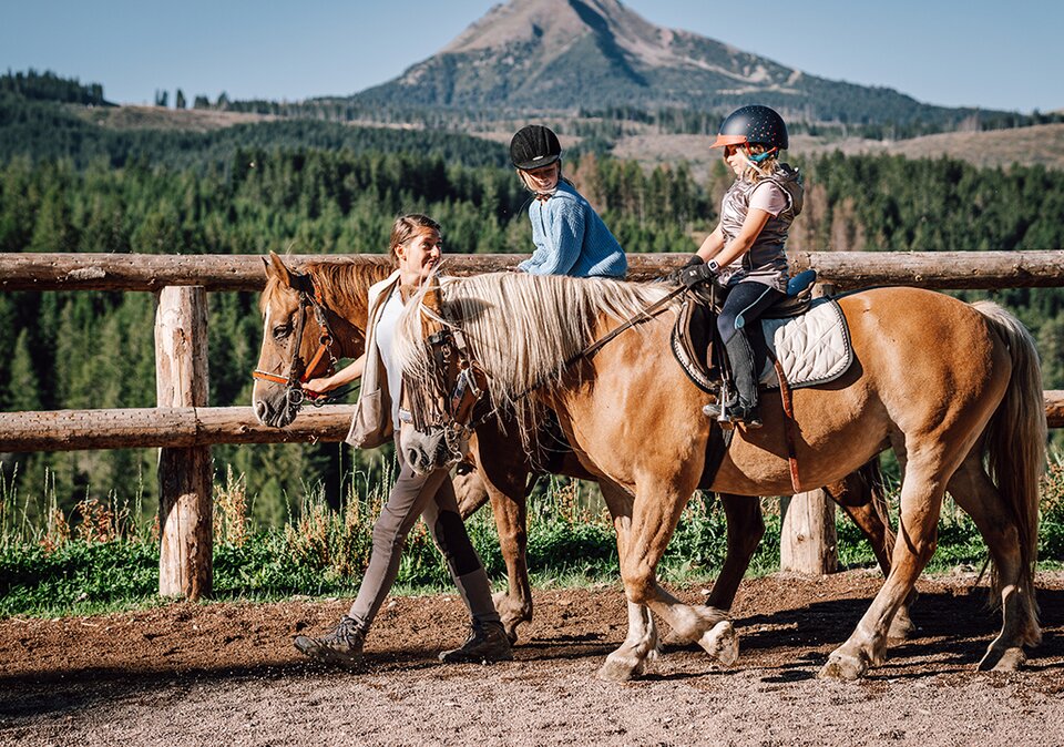 Instructor guiding children on horses at mountain riding arena