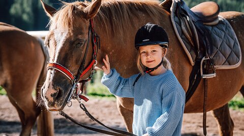 Girl in blue sweater standing next to her brown horse
