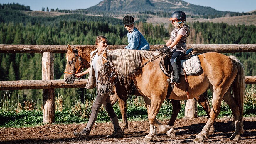 Instructor guiding children on horses at mountain riding arena