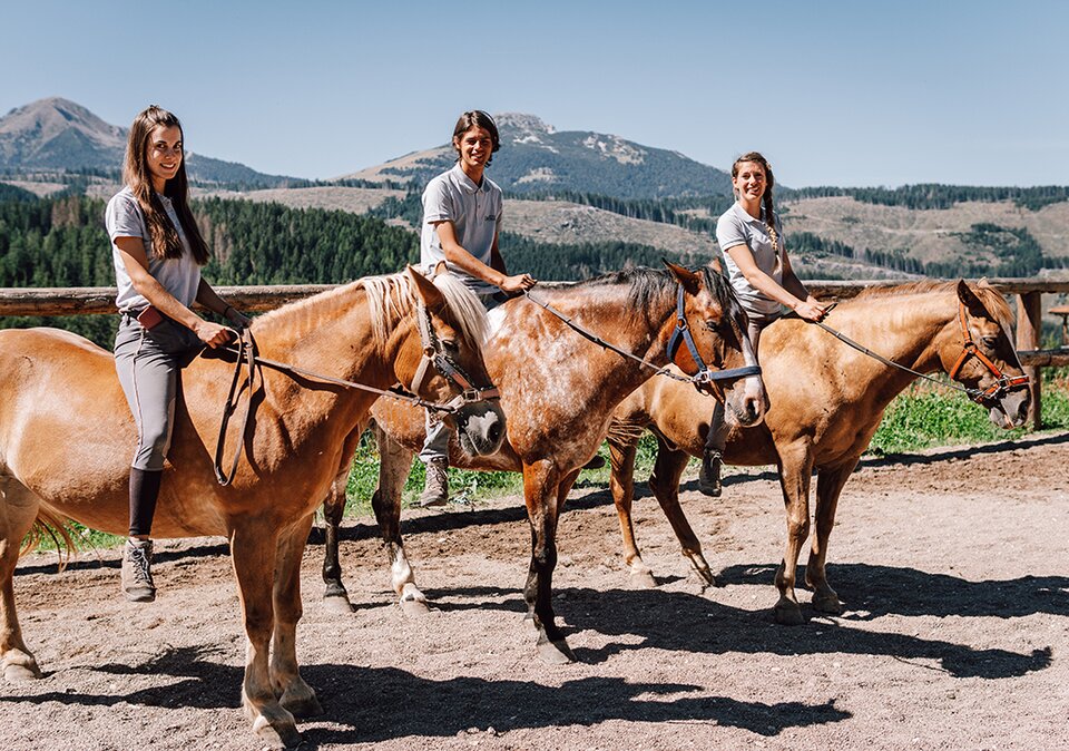 Three riding instructors smiling on their horses with mountains in the background