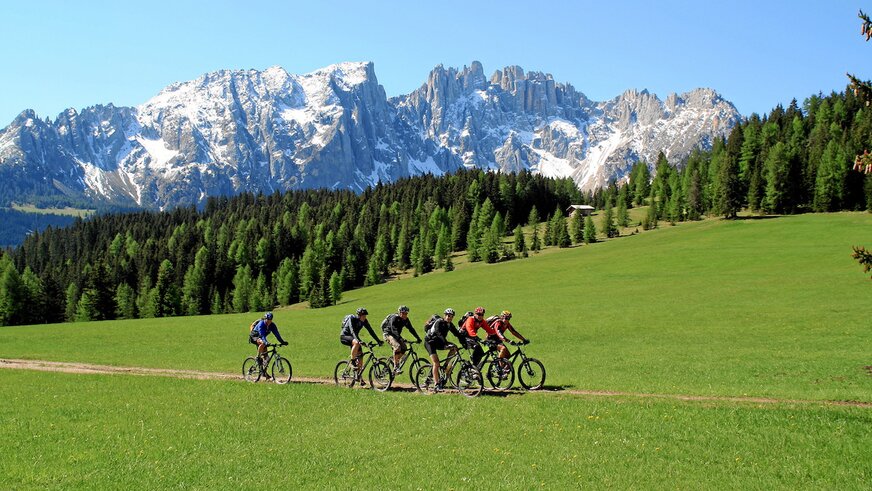 Un gruppo di ciclisti pedala su un sentiero con le Dolomiti innevate sullo sfondo