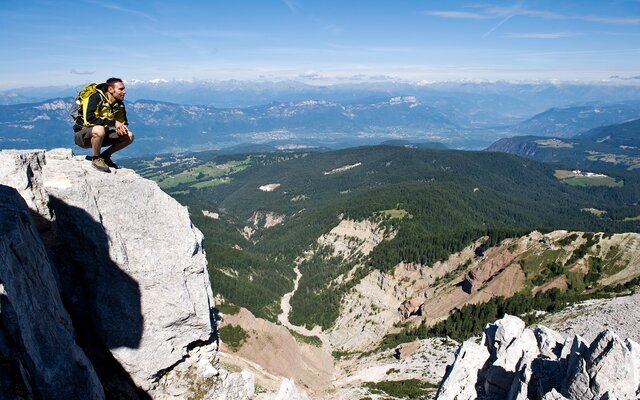 Escursionista accovacciato su una roccia con vista panoramica