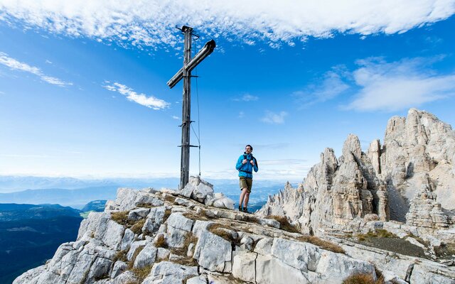 Escursionista accanto a una croce di vetta con vista sulle montagne