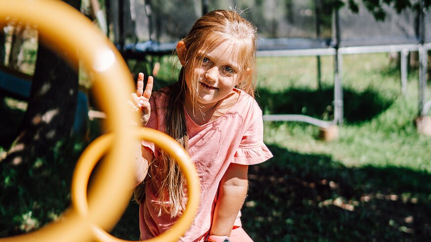 Smiling girl playing outdoors near a trampoline.
