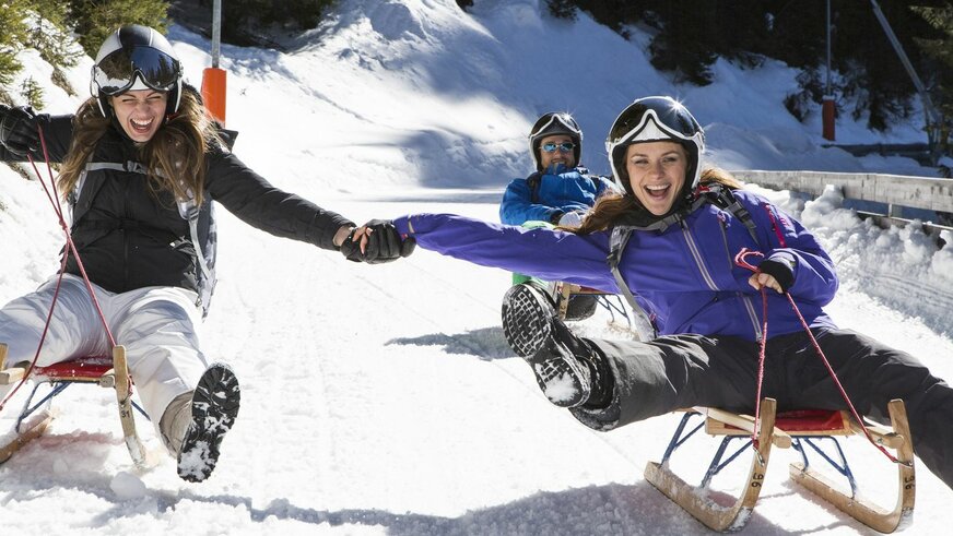 Three people enjoying a sled ride on the snow.