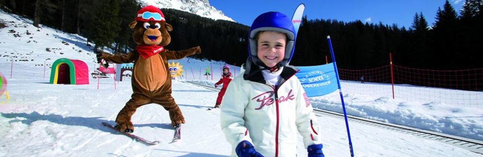 Ski scene with children and a mascot bear on the snow.