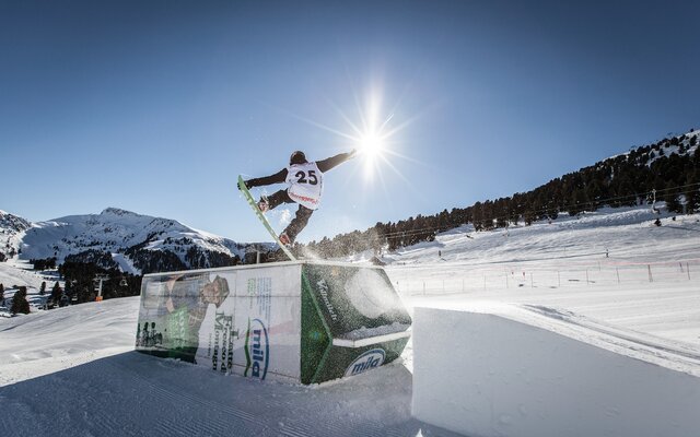 A snowboarder performs a jump over an obstacle in the snow park.