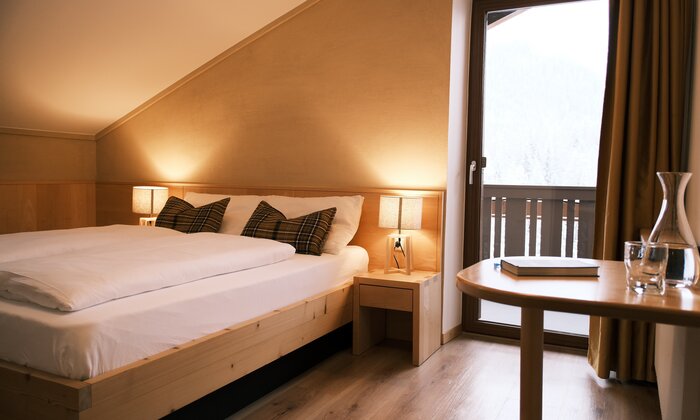 Letto in legno con biancheria bianca, finestra e arredo moderno.